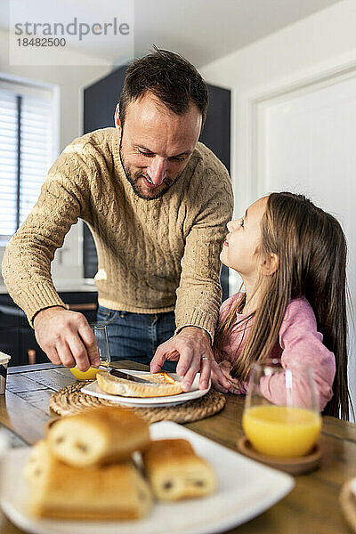 Lächelnder Vater serviert seiner Tochter am Tisch Frühstück