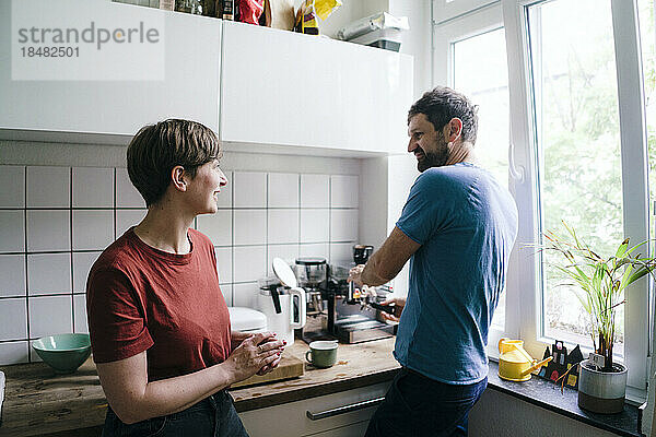 Frau spricht mit Mann  der zu Hause in der Küche Kaffee zubereitet