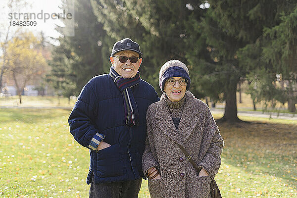 Lächelndes älteres Paar mit den Händen in den Taschen  das im Park steht