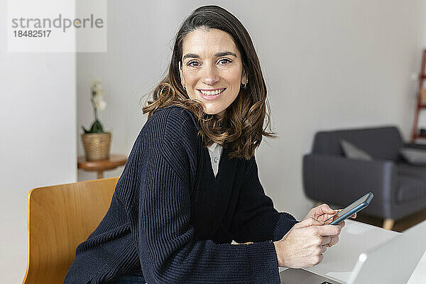 Glückliche Geschäftsfrau mit Smartphone sitzt im Büro
