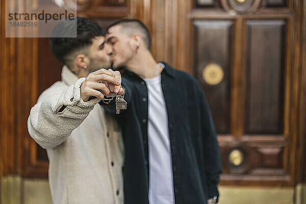 Liebevolles schwules Paar mit Hausschlüssel  das sich vor der Tür küsst