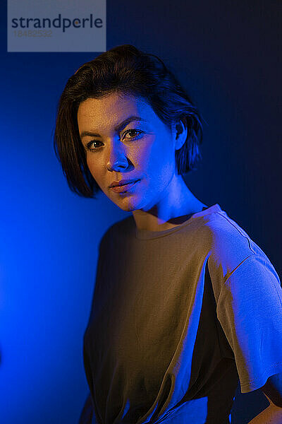 Selbstbewusste Frau mit kurzen Haaren in Neonbeleuchtung vor farbigem Hintergrund