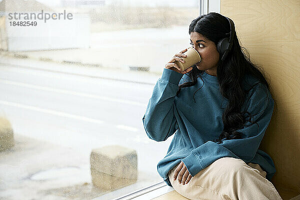 Frau trinkt Kaffee und sitzt am Fenster