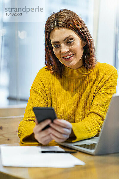 Lächelnde Geschäftsfrau benutzt Smartphone am Tisch im Café