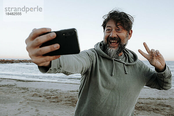 Glücklicher reifer Mann  der am Strand ein Selfie per Smartphone macht