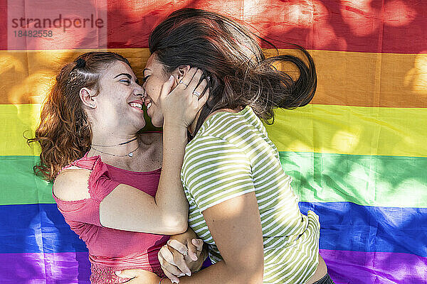Liebevolles lesbisches Paar  das auf einer regenbogenfarbenen Flagge liegt