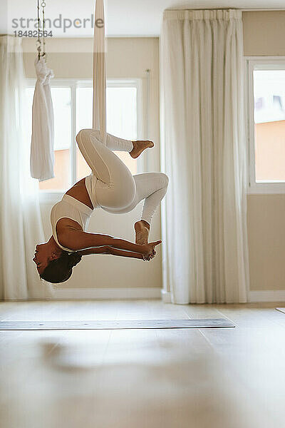 Frau macht Aerial Yoga und hängt in der Hängematte im Studio