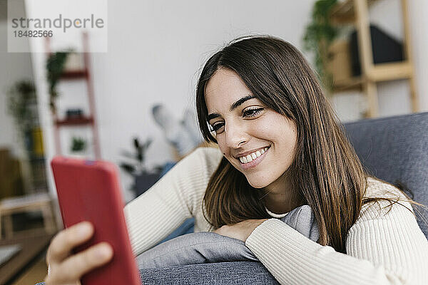 Glückliche Frau  die SMS über ihr Smartphone im Wohnzimmer sendet