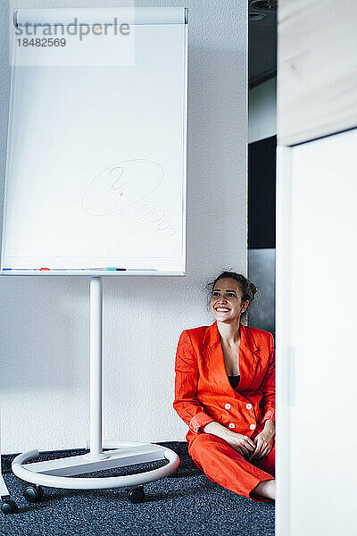 Nachdenkliche junge Geschäftsfrau sitzt am leeren Flipchart im Büro