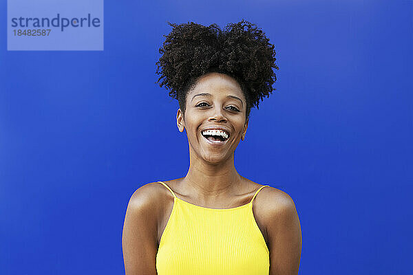 Junge Frau mit Afro-Frisur lacht vor blauem Hintergrund