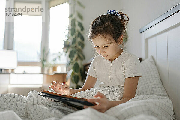 Mädchen sitzt im Schlafzimmer und benutzt Tablet-PC