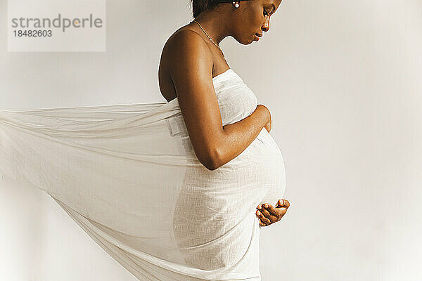 Junge schwangere Frau mit weißem Laken bedeckt vor der Wand