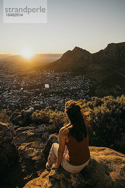 Frau sitzt auf einem Felsen und blickt vom Lion's Head Mountain auf das Stadtbild