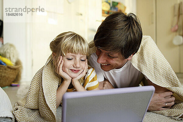 Lächelnder Vater und Tochter schauen zu Hause auf den Tablet-PC  der auf dem Boden liegt