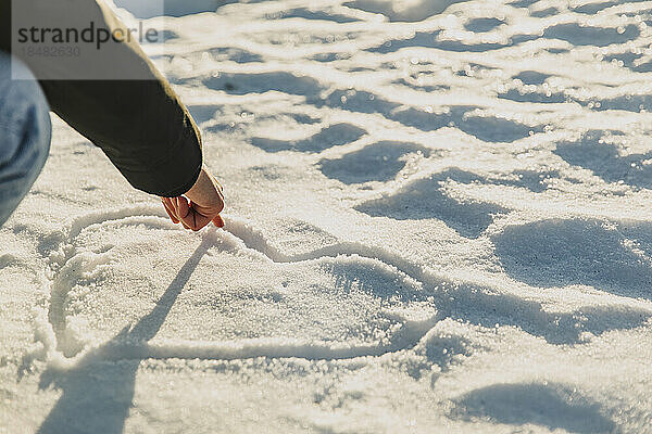 Frau zeichnet im Winter Herzform auf Schnee