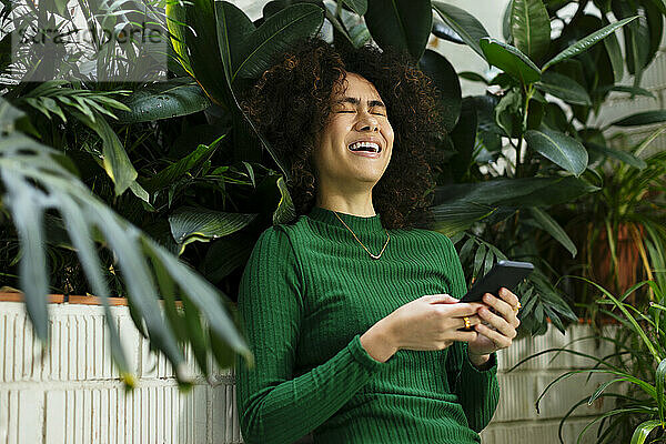 Fröhlicher Freiberufler mit Smartphone sitzt inmitten von Pflanzen
