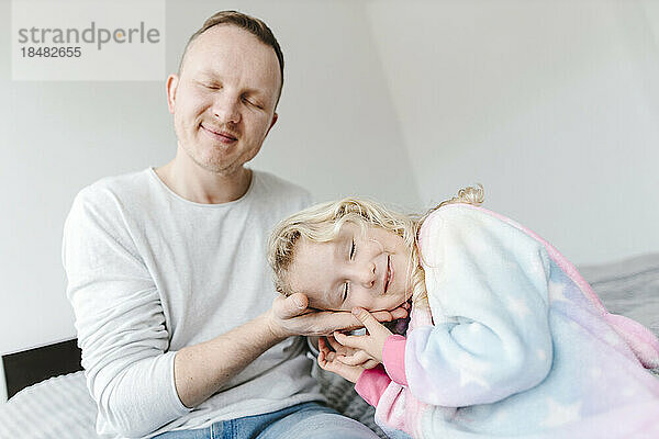 Smiling daughter leaning head on fathers hand at home