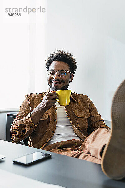 Glücklicher Geschäftsmann sitzt mit Kaffeetasse im Büro