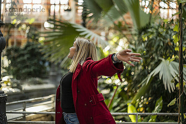 Carefree mature woman with arms outstretched standing in front of plants