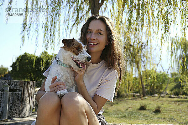 Glückliche junge Frau sitzt mit süßem Hund im Park