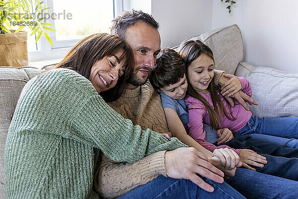 Lächelnde Frau umarmt Familie zu Hause auf dem Sofa