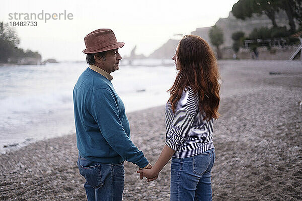 Paar hält Händchen und steht am Strand