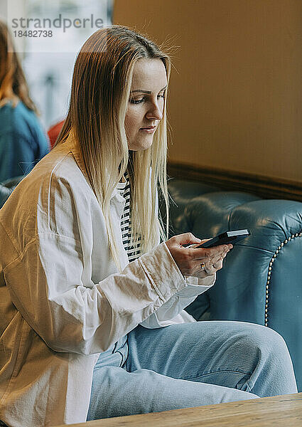 Frau sitzt mit Smartphone auf der Couch im Café