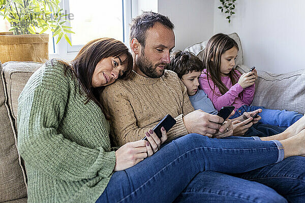 Mann und Frau mit Kindern nutzen Smartphone zu Hause