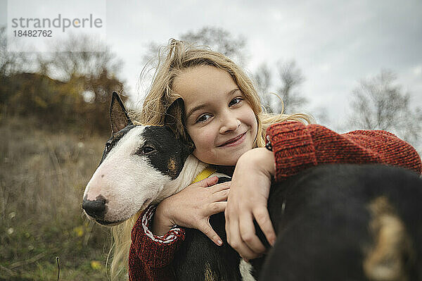 Lächelndes süßes Mädchen  das Hund umarmt