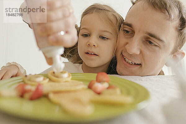 Glücklicher Vater und Tochter dekorieren zu Hause Pfannkuchen auf dem Teller