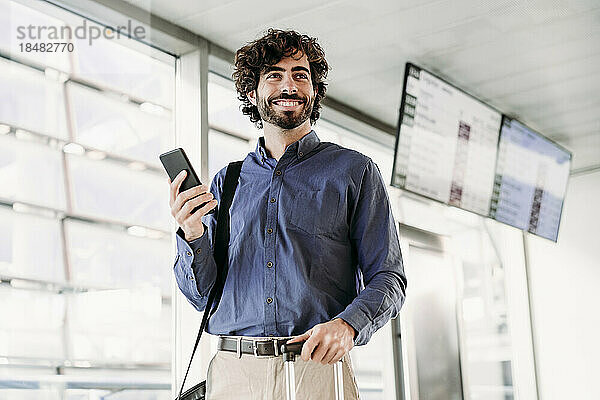 Glücklicher Geschäftsmann steht mit Mobiltelefon am Bahnhof