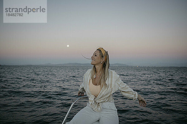 Glückliche Frau sitzt bei Sonnenuntergang auf einem Boot im Meer