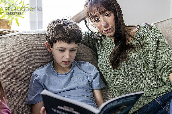 Woman reading book with son on sofa at home
