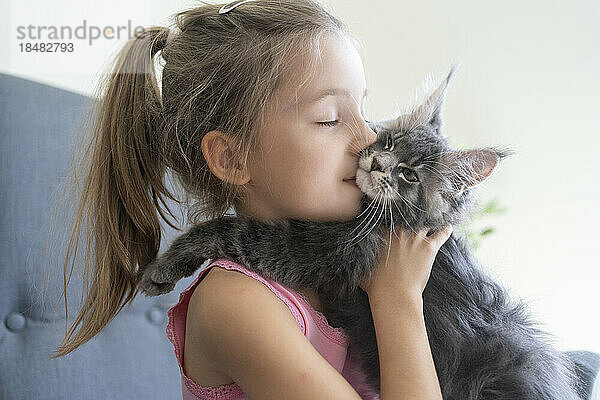 Mädchen mit geschlossenen Augen küsst Katze zu Hause