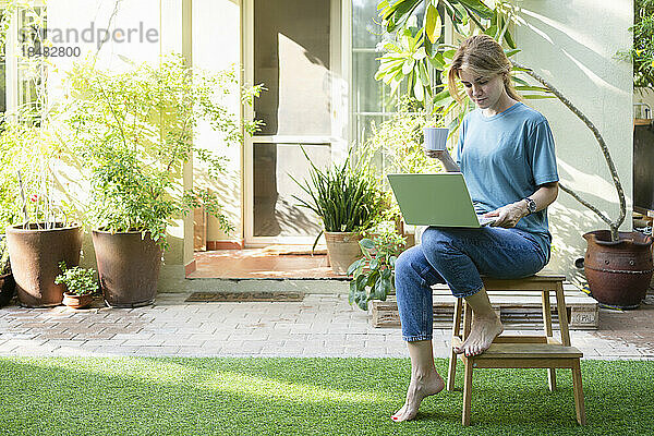 Freiberufler mit Kaffeetasse und Laptop sitzt im Garten