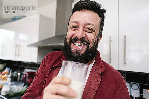 Glücklicher Mann hält ein Glas Milch in der heimischen Küche