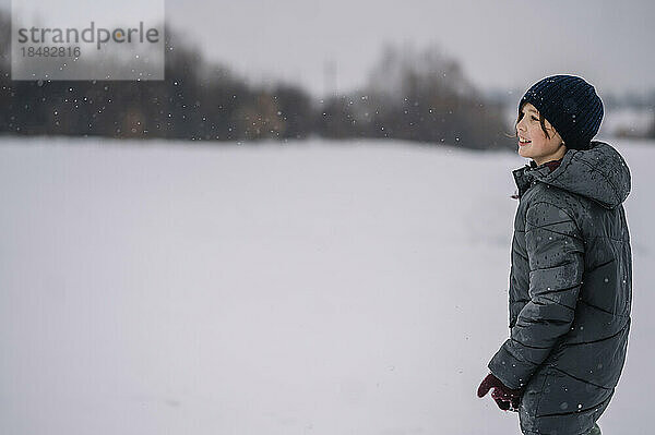 Lächelnder Junge mit Strickmütze steht im Schnee
