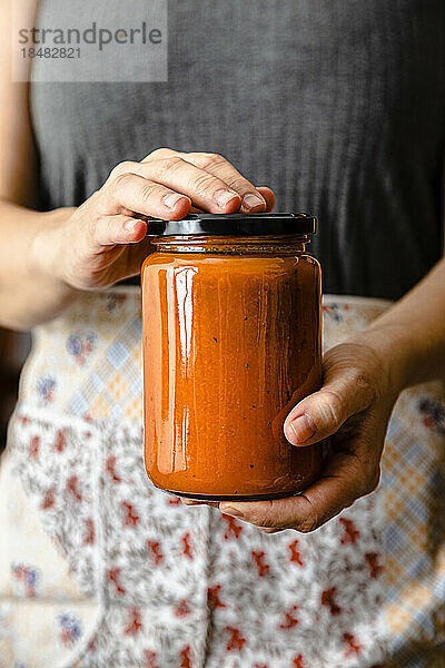 Hände einer reifen Frau  die ein Glas mit selbstgemachter Tomatensauce hält