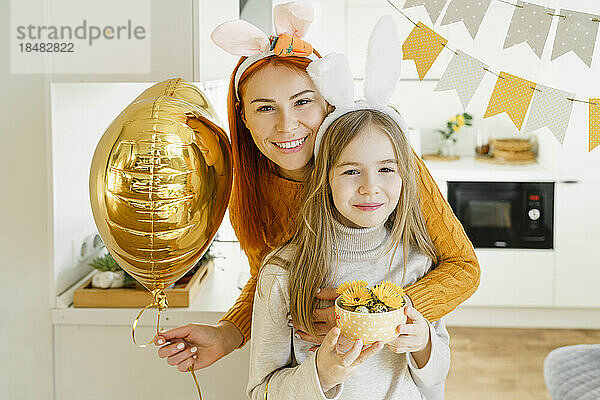 Glückliches Mädchen mit Mutter  die zu Hause einen Ballon feiert und Ostern feiert