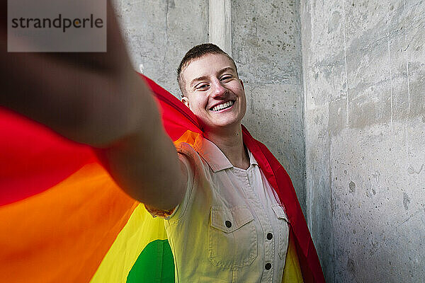 Fröhliche nicht-binäre Person  die ein Selfie mit Regenbogenfahne macht