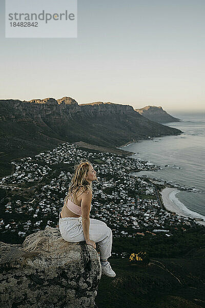 Frau sitzt bei Sonnenaufgang auf einem Felsen am Stadtbild