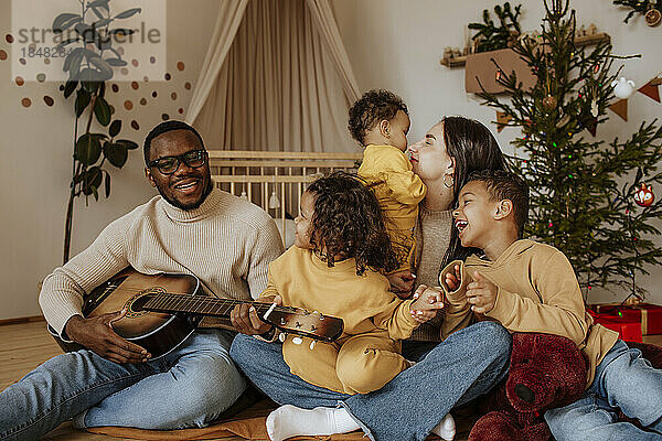Fröhliche Familie verbringt zu Weihnachten Zeit miteinander und spielt Gitarre
