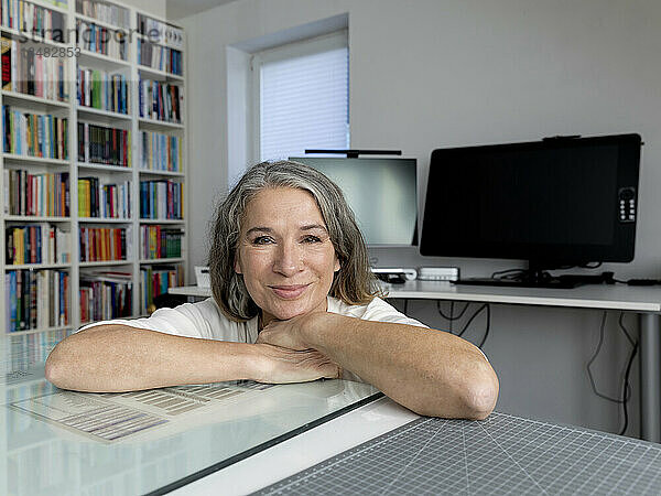 Smiling senior businesswoman leaning on desk in office