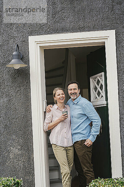 Fröhliches älteres Paar steht am Eingang des Hauses