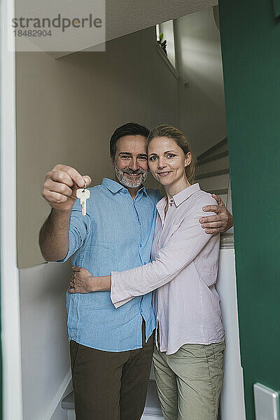 Lächelnde Frau mit Ehemann  der zu Hause den Hausschlüssel hält