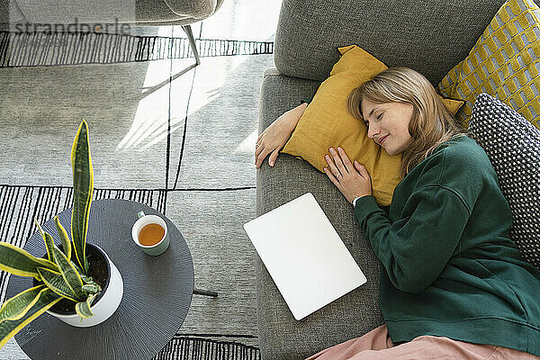 Lächelnde Frau entspannt sich zu Hause auf dem Sofa