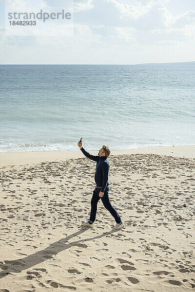 Mann filmt mit Smartphone und spaziert am Strand entlang der Küste
