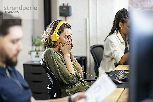 Geschäftsfrau mit Kopfhörern sitzt vor dem Schreibtisch im Büro