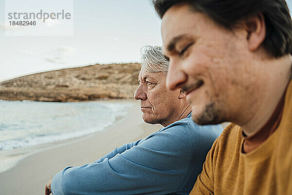 Lächelnder Mann sitzt mit Vater am Strand