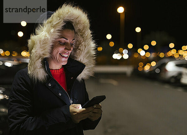 Glückliche Frau  die nachts mit dem Mobiltelefon im Internet surft